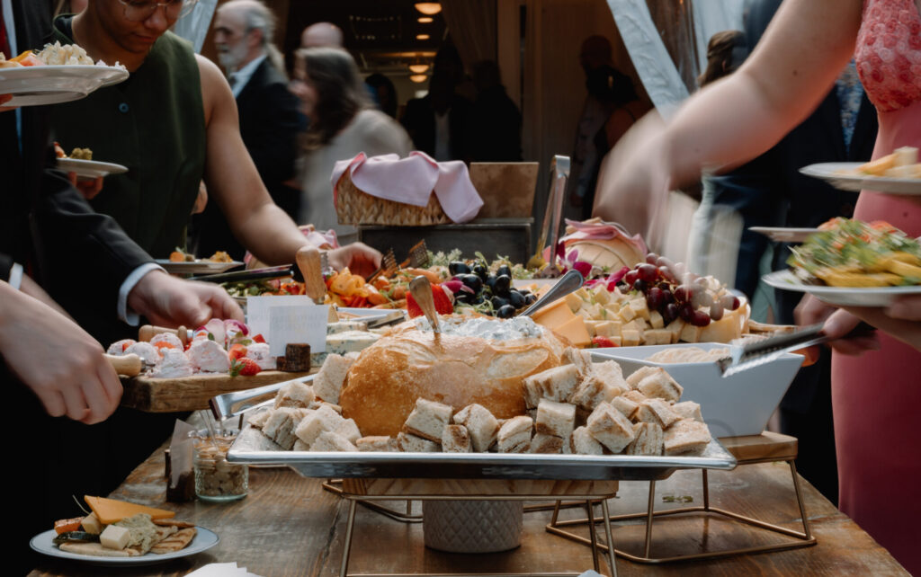 Wedding guests taking food off of a cocktail hour grazing table at Flourtown Country Club